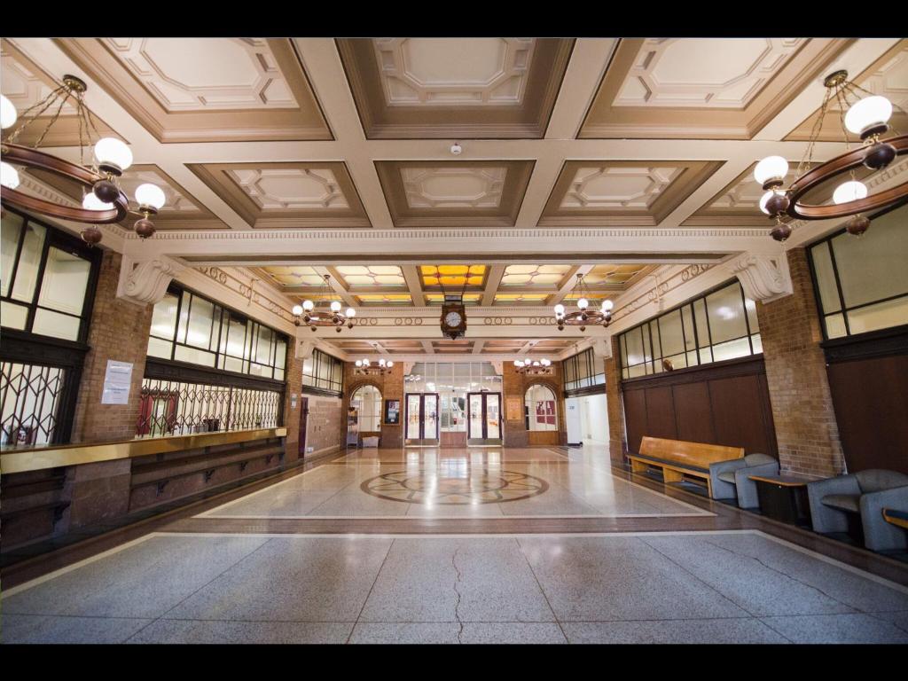 The original booking hall in use as the hotel lobby: brick pillars, a long timber counter, chandeliers and a clock set into amber stained glass above the doors.