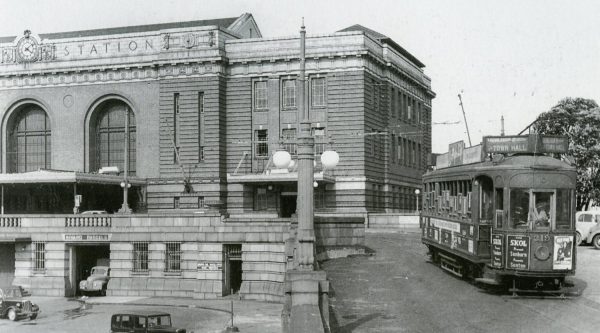 Historic Auckland Railway Station with a tram passing the Town Hall platform outside.
