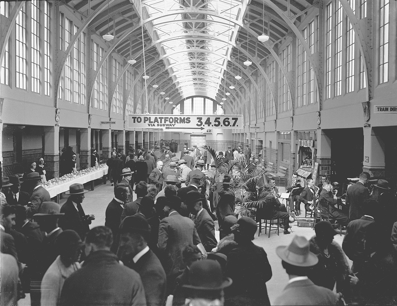 Historic black-and-white view of the station hall filled with passengers and musicians.