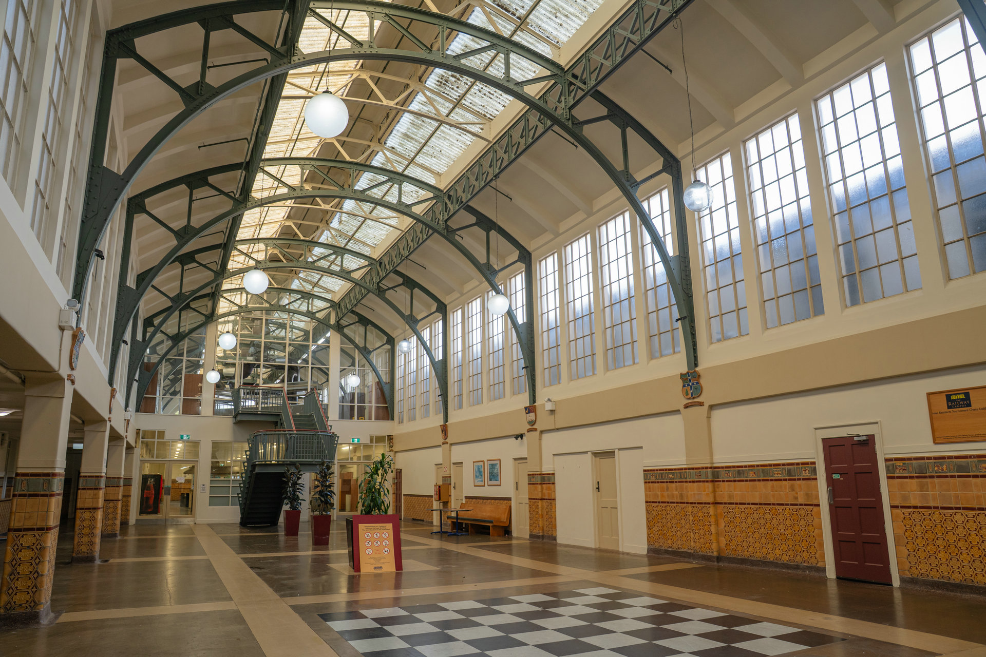 The Grand Hall's green steel arches and glazed roof above a chequerboard floor and patterned tiled walls.