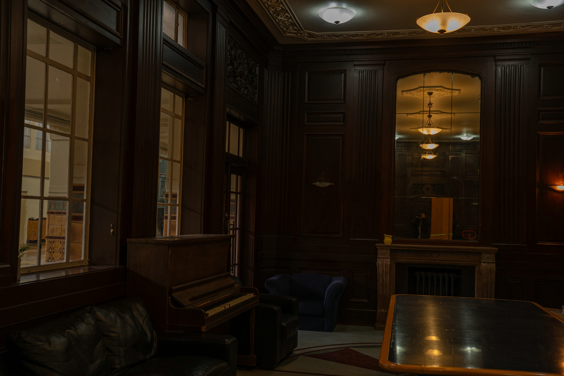 A dark timber-panelled room with an upright piano, leather armchairs and a marble fireplace.