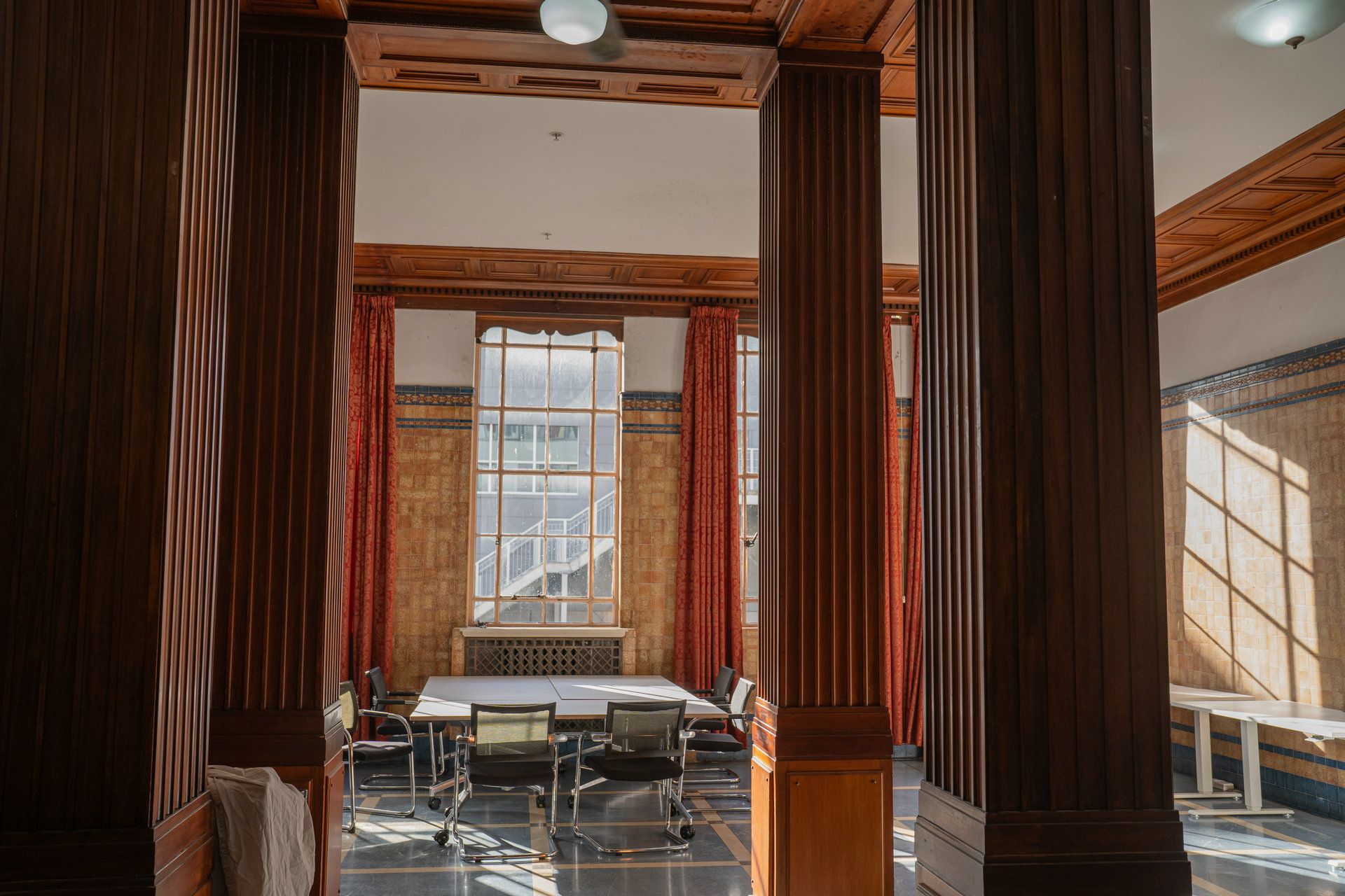 Polished timber columns framing a meeting table, with afternoon light across the tiled walls.