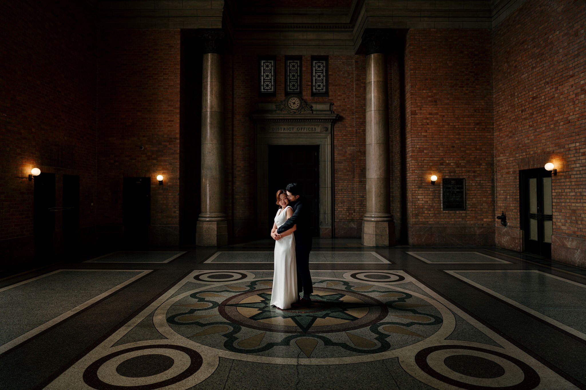 A couple embracing beneath the clock and stone columns of the Grand Foyer.